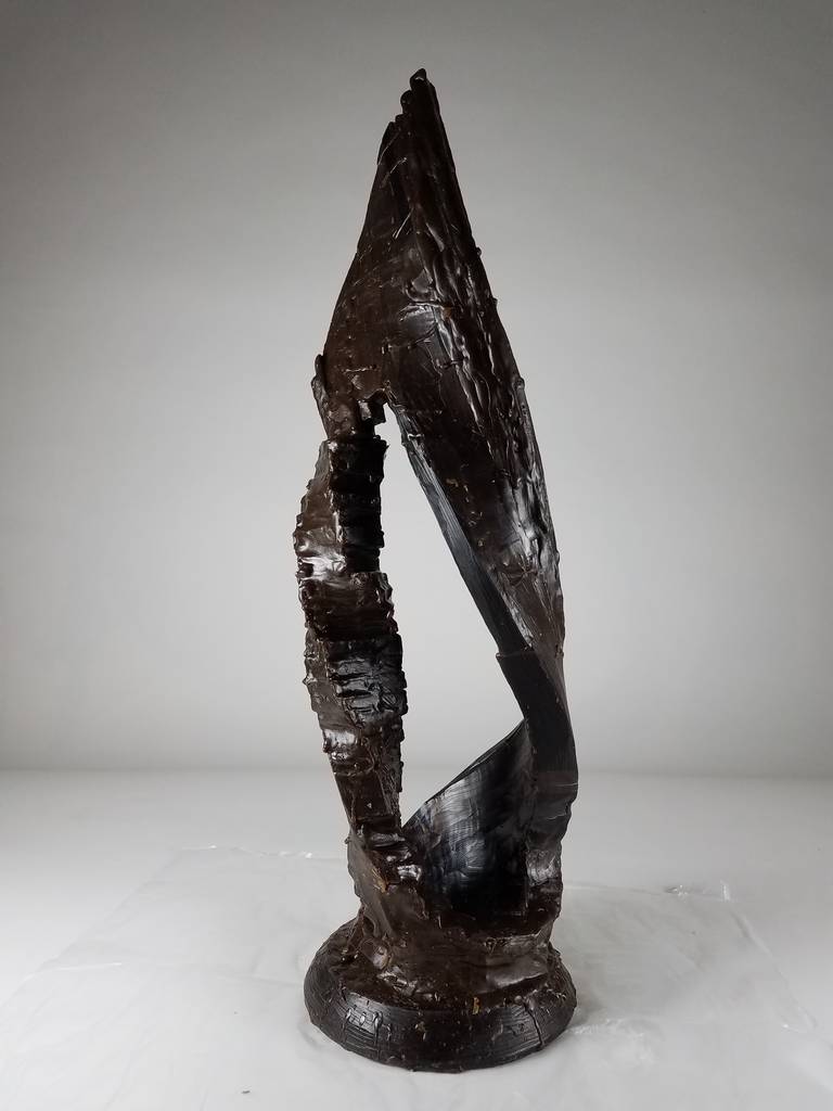 Dark brown wax form with vague resemblance to the ultimate sculpture. Large negative space framed by twisted structure on left and bent arch on right.